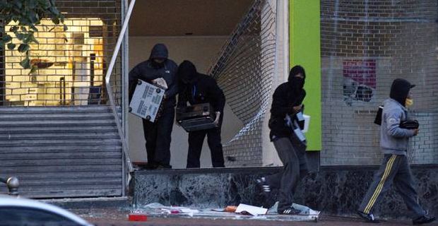 A group of looters in black hoodies steal merchandise from a store.