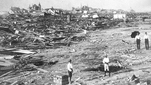 A black and white photo of men standing among the wreckage left by the Galveston hurricane of 1900.