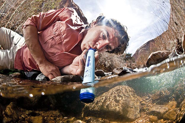 A man drinking from a river using a LifeStraw water filter.
