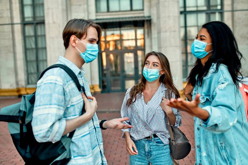 A group of students wearing protective medical masks talk outside the campus-Back to School Preparation