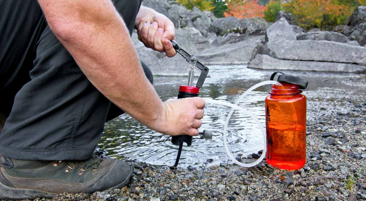 A person uses a lightweight compact water filter to pump safe drinking water | How To Collect And Store Water For Survival And Off Grid Living