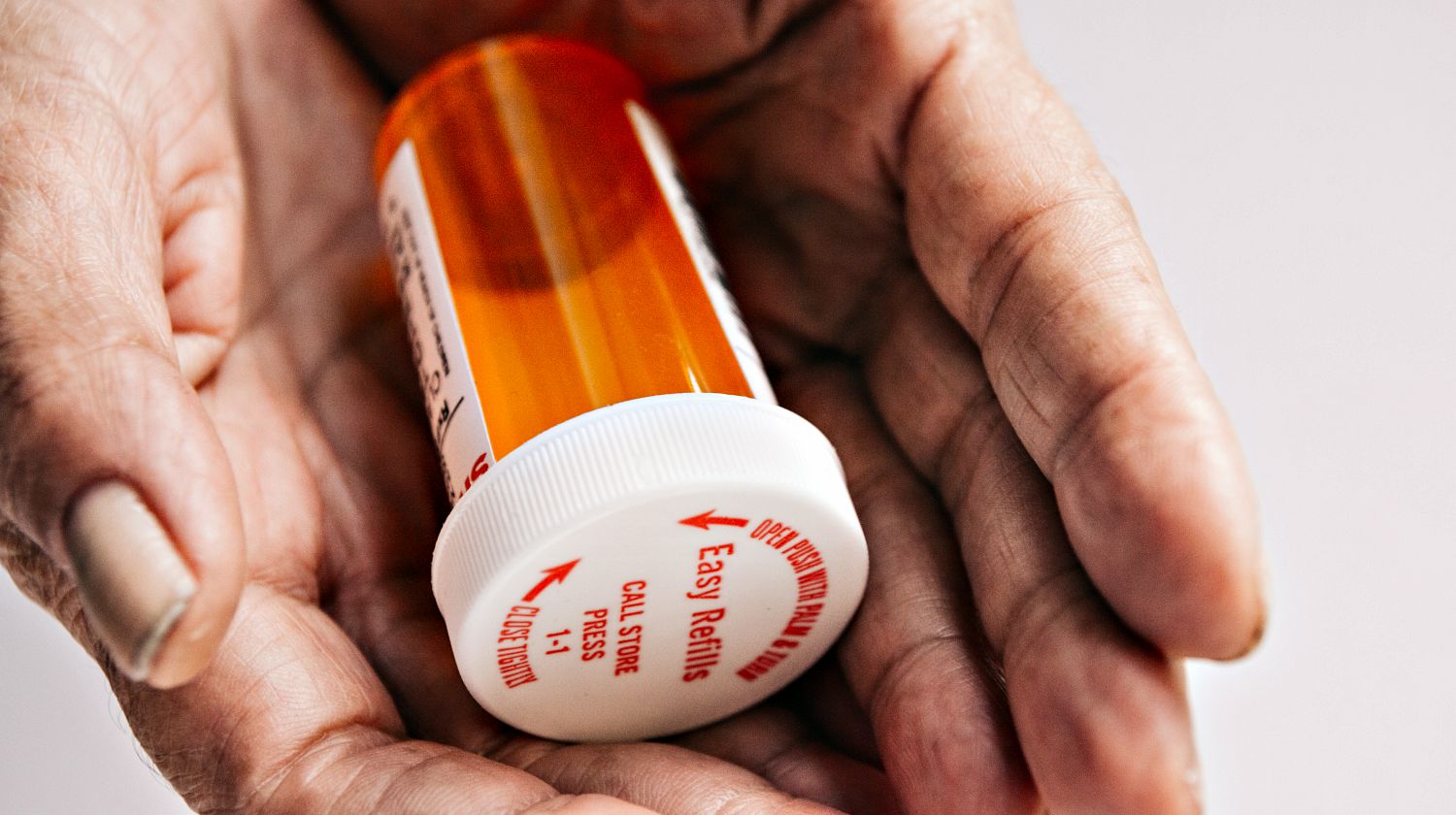 Feature | Wrinkled old lady hands holding a bright red orange prescription medication pill bottle | DIY Pill Bottle Fire Starter