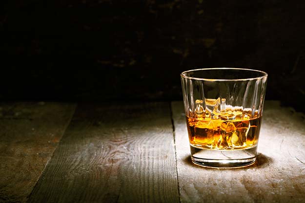 A tumbler of whiskey on the rocks sitting on a bar.