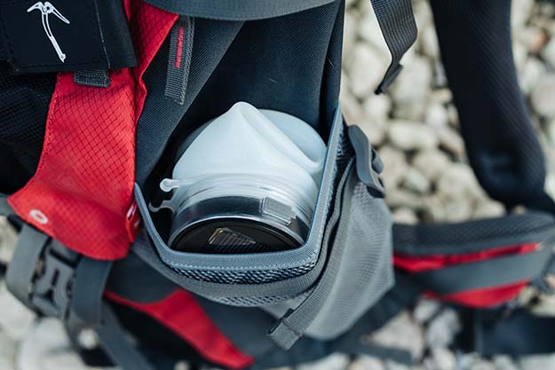 Stone Mountain AquaLight water bottle crushed into the side pocket of a red backpack.