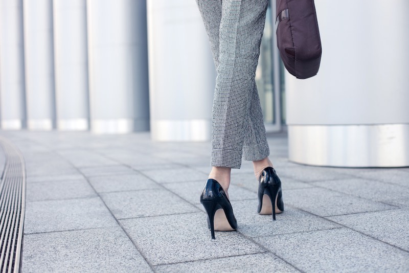 Close up of female legs of worker standing near her office. The woman is wearing formalwear and shoes on high heels. She is holding a handbag. Copy space in left side | lady's technique