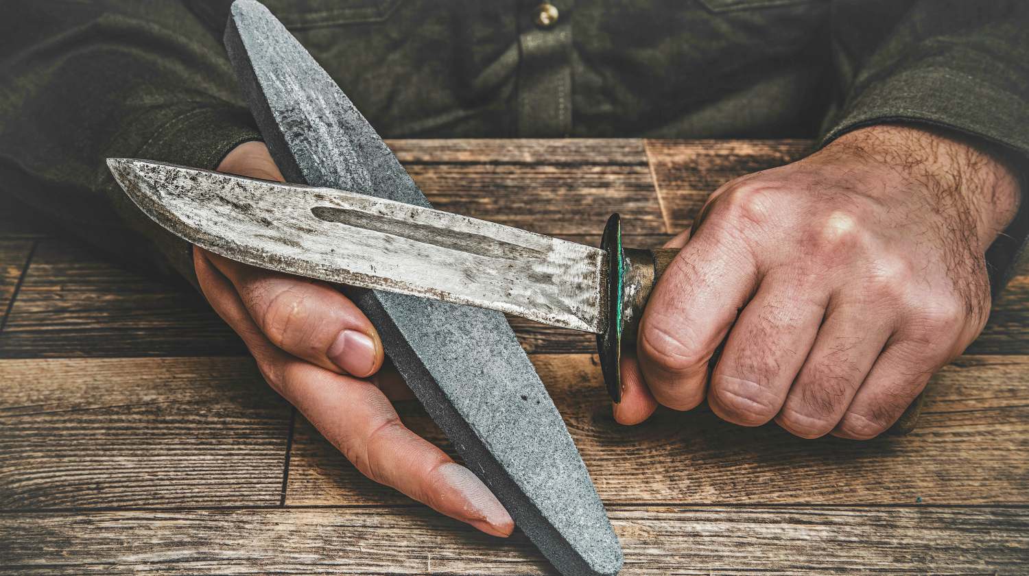 Feature | Man's hands sharpening old knife on the wooden table | Tricks For Better Knife Sharpening