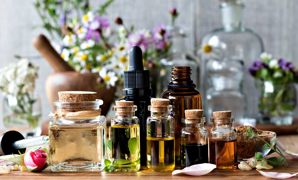 Selection of essential oils, with herbs and flowers in the background | Ways To Remove A Splinter