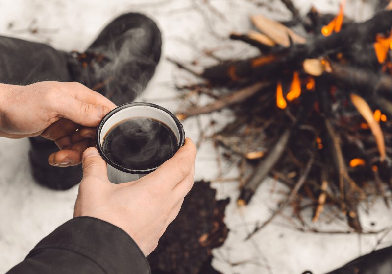 male hands hold mug coffee near | how to start a fire in the woods