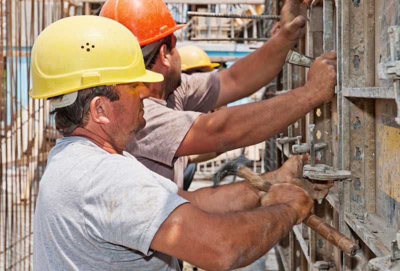 Authentic construction workers positioning in place cement formwork frames
