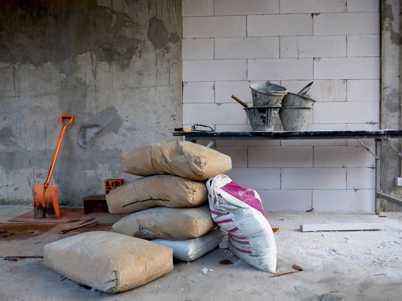 The bags of cement , orange shovel and cement tub on table with block bricks wall in the construction site