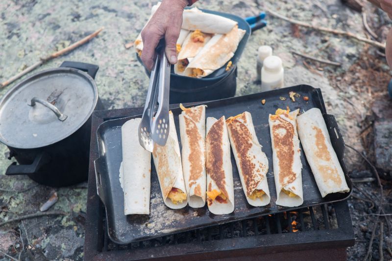 young-man-cooking-over-camp-fire | campfire burrito
