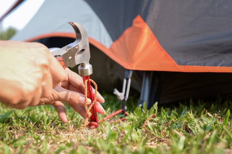 young-woman-fastening-tent-holding-hammer camping tents SS