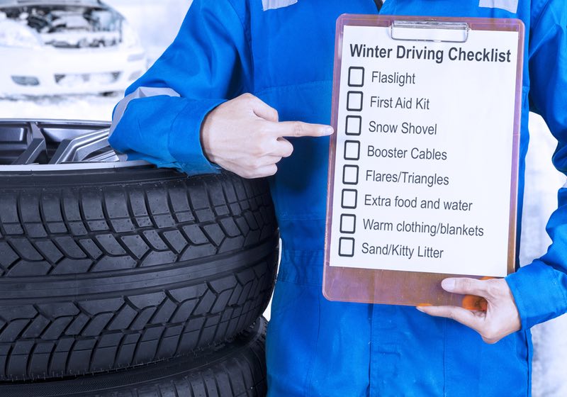 car mechanic leaning on a pile of tires and showing a winter driving tips on the clipboard | winter driving tips | winter driving checklist