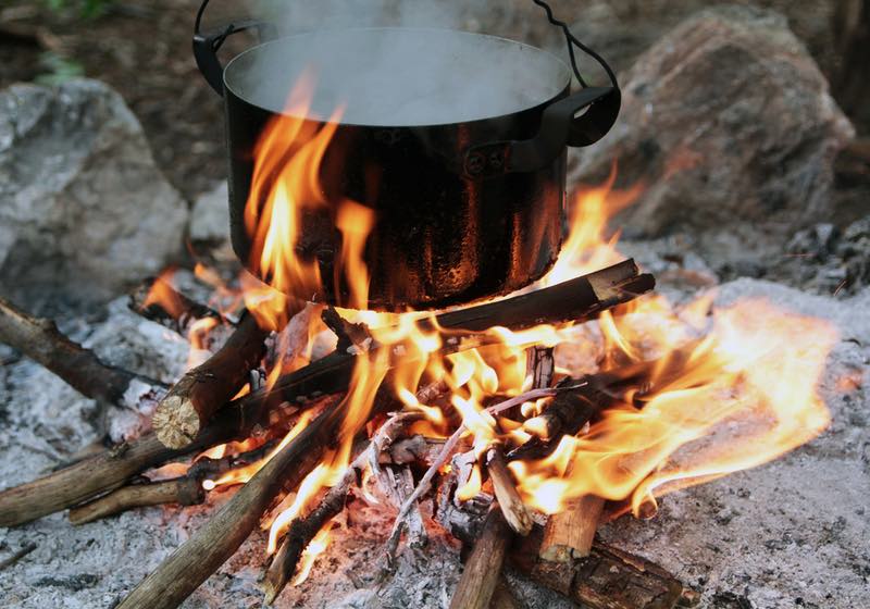a pot of water boiling over a fire and a flame. Preparing food on campfire in wild camping | campfire cooking