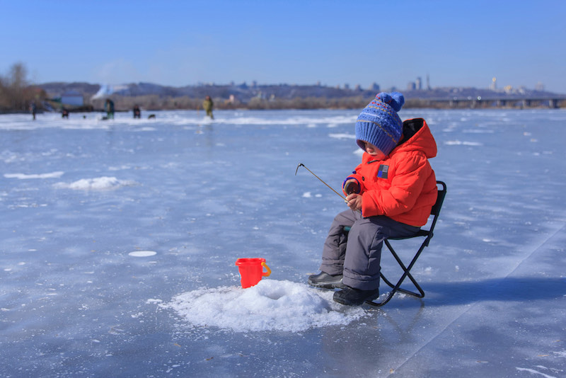 a little boy in winter clothes is fishing on a frozen lake | ice fishing tips
