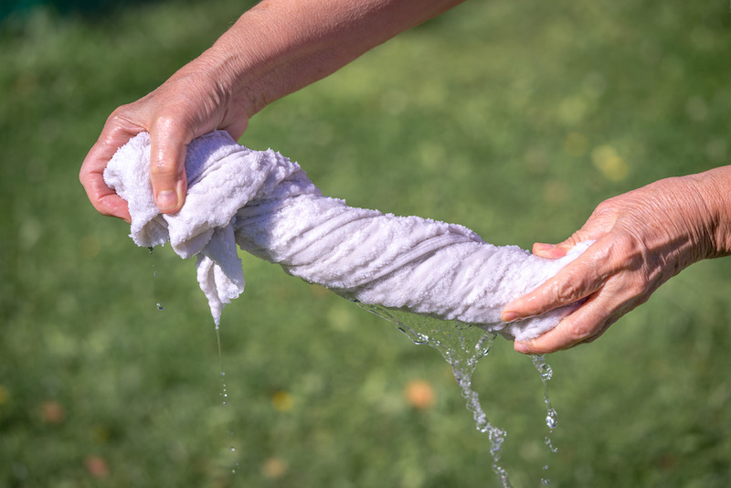 Hands squeeze wet fabric on a grass background | dew bottled