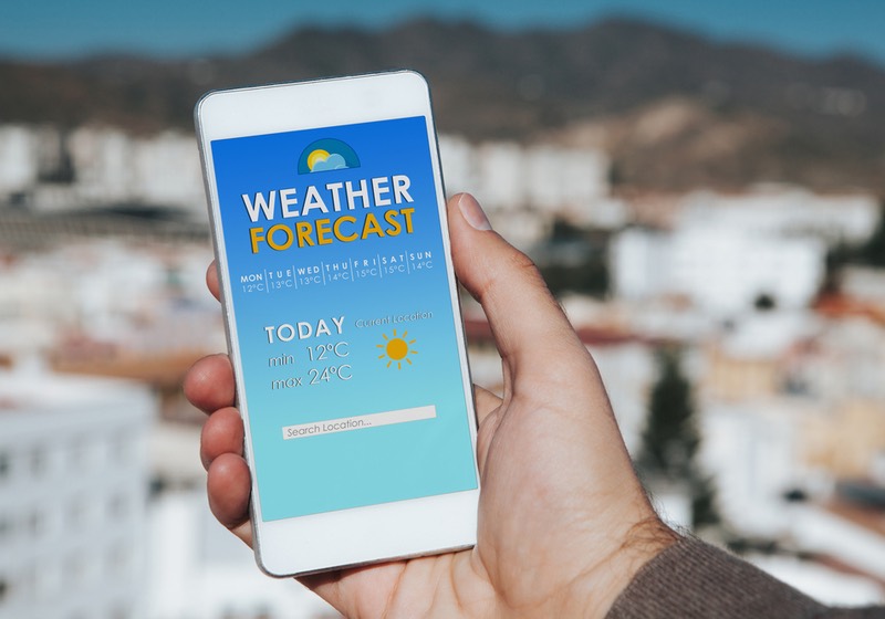 Weather forecast mobile phone app while man hold the smart phone in the hand, with the city in the background. | check weather forecast