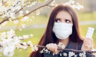 Woman with Respirator Mask Fighting Spring Allergies Outdoor - Portrait of an allergic woman surrounded by seasonal flowers wearing a protective mask | spring allergies