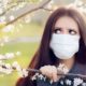 Woman with Respirator Mask Fighting Spring Allergies Outdoor - Portrait of an allergic woman surrounded by seasonal flowers wearing a protective mask | spring allergies