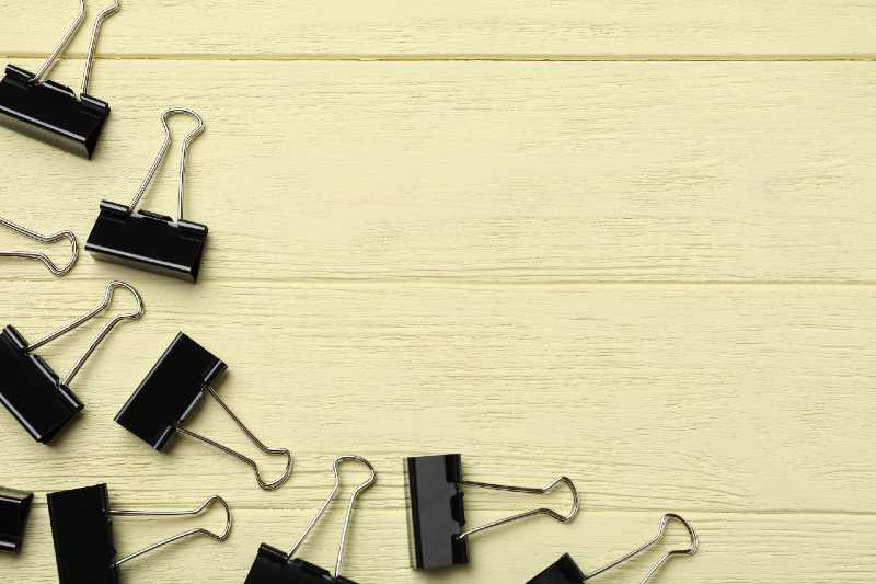Black binder clips on yellow wooden table, flat lay. Space for text-binder clips