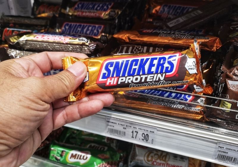 Hand pick up a packed of SNICKERS HI PROTEIN Foods to stock up on SS
