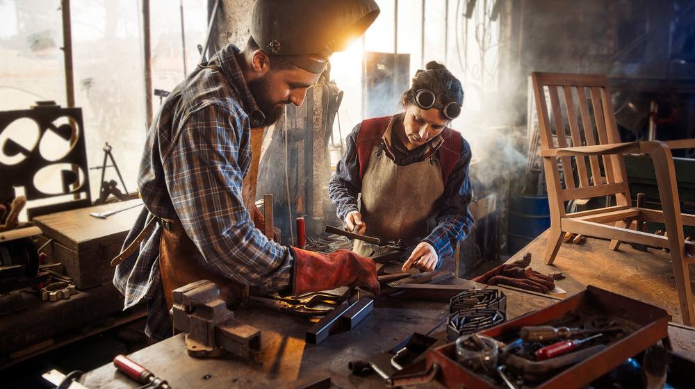 Two artisans welder in their craft workshop welding metal parts to assemble them on a designer wooden armchair. A man and a woman | How To Make A War Hammer | Featured