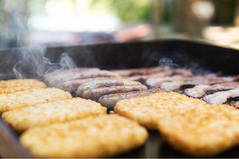 Bacon, sausage and hasbrowns cooking on a grill for breakfast at camp-favourite camping recipes
