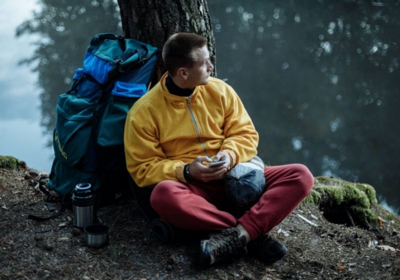 Man in yellow sweater and red pants sitting on ground | camping in the rain hacks