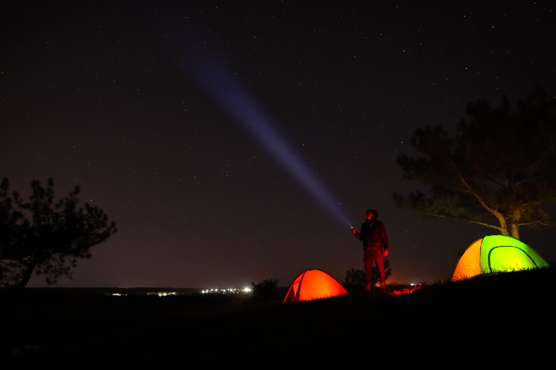Man with bright flashlight near camping tents outdoors at night-Camping Without Electricity