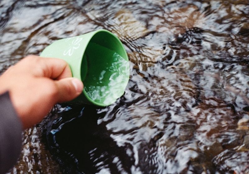 Person scooping water using green cup Car camping essentials PX