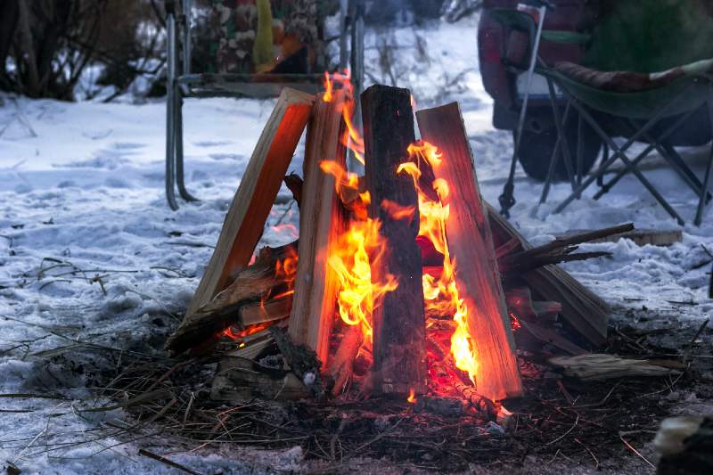 Red flames of teepee campfire on snowy ground at campsite-Types of Campfires