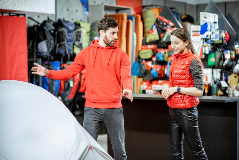 Salesman selling camping equipment to a young woman client in the sport shop | best camping tents