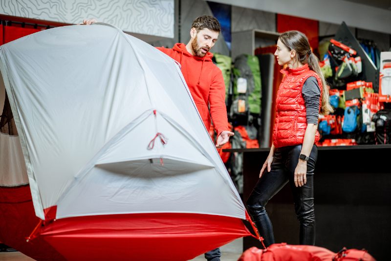 Salesman selling camping equipment to a young woman client in the sport shop-tent