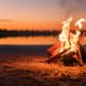 Small campfire with gentle flames beside a lake during a glowing sunset | The 5 Most Basic Types of Campfires And What They're For | featured
