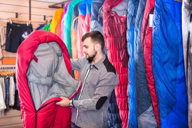 Smiling guy deciding on new sleeping bag at a sports equipment store-sleeping bag