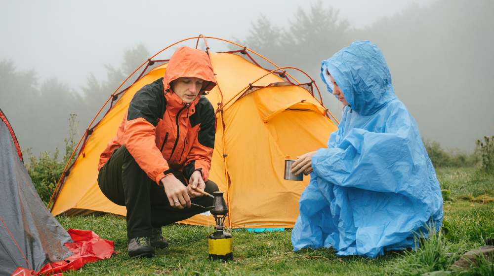 Tourists cooking coffee on primus near the tent in the mountains. Foggy and rainy camping while hiking | 5 Useful Tips For Camping In The Rain | featured