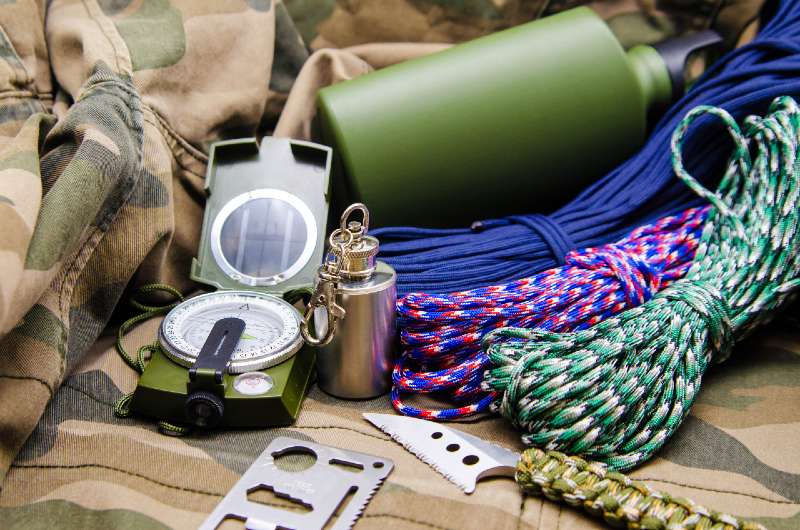 Travel accessories survival kit tools. Compass, metal flask, knife and colored paracord on the camouflage background-summer hunting