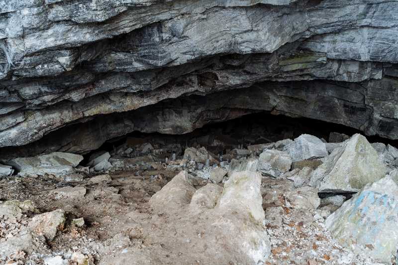 a stone entrance to the cave. karst failure in the ground. dark black hole deep in the cave-terrain