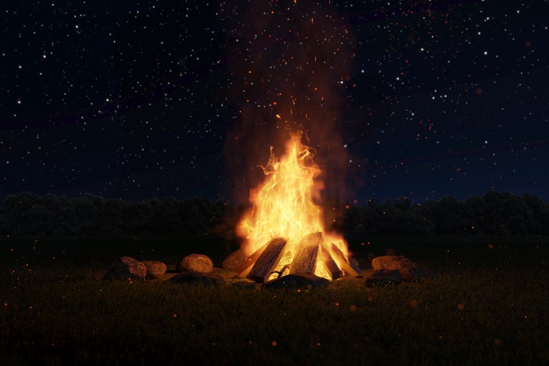 big bonfire with sparks and particles in front of forest and starry sky-Types of Campfires