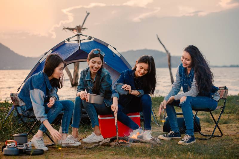 A group of young women camping, they sit around the fire-Camping With A Large Group