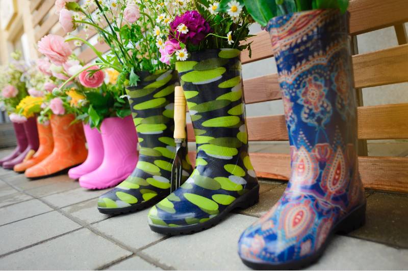 Gardening. Colourful rubber boots with bouquets of flowers in them stand in a row. Garden decor. Rain boots with flowers in a row-Small Space Garden