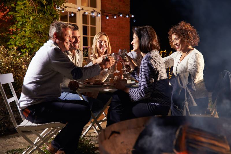 Mature friends enjoying an outdoor dinner around the fire pit