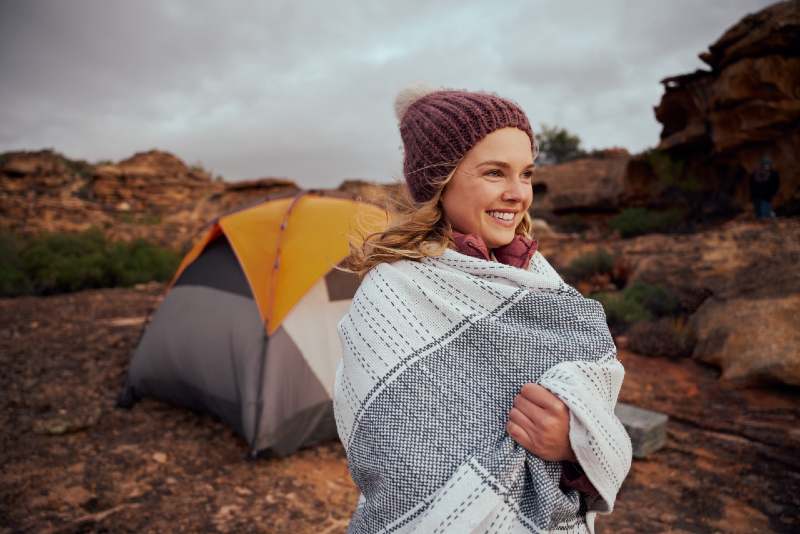 Woman with blanket wrapped in winter hat looking away while camping without electricity