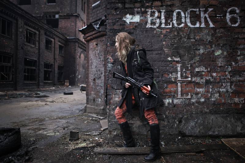Young survivor armed woman looking out of corner of building with rifle in hands preparing for shtf