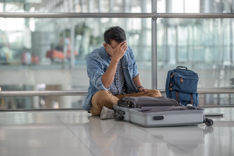 Young traveler in casual clothes, sitting on the floor at the terminal airport, unpacking luggage, losing problem passport while preparing for vacation for Shtf