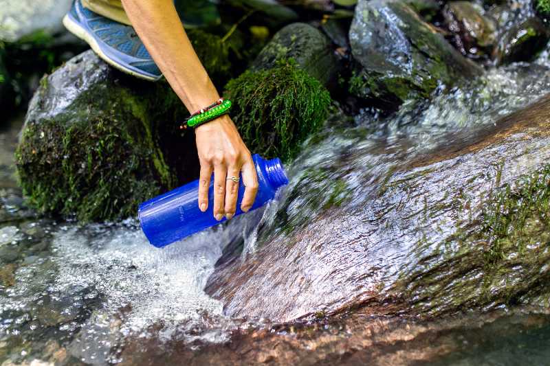 beautiful woman taking water from a forest spring on a hike - camping without electricity