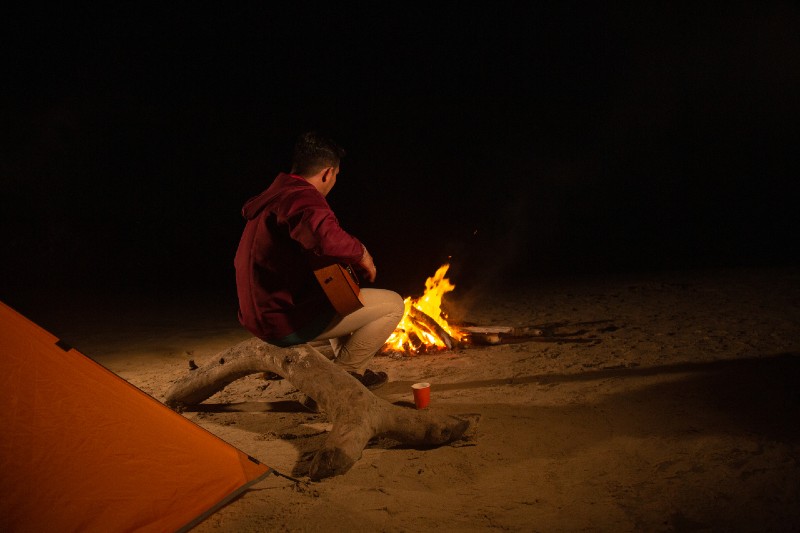 Man camping alone on the beach, accompanied by a campfire and guitar camping alone