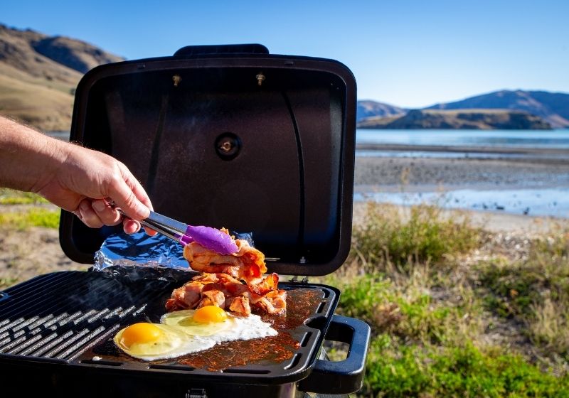 A man cooks bacon and eggs on a portable bbq | Top 10 Best Portable Camping Grills