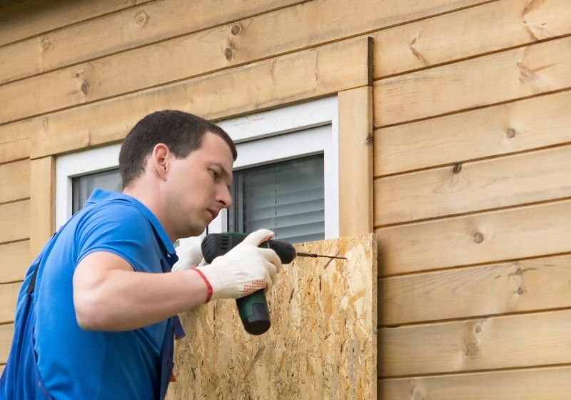A man fastens a plywood sheet | hurricane preparedness check list 