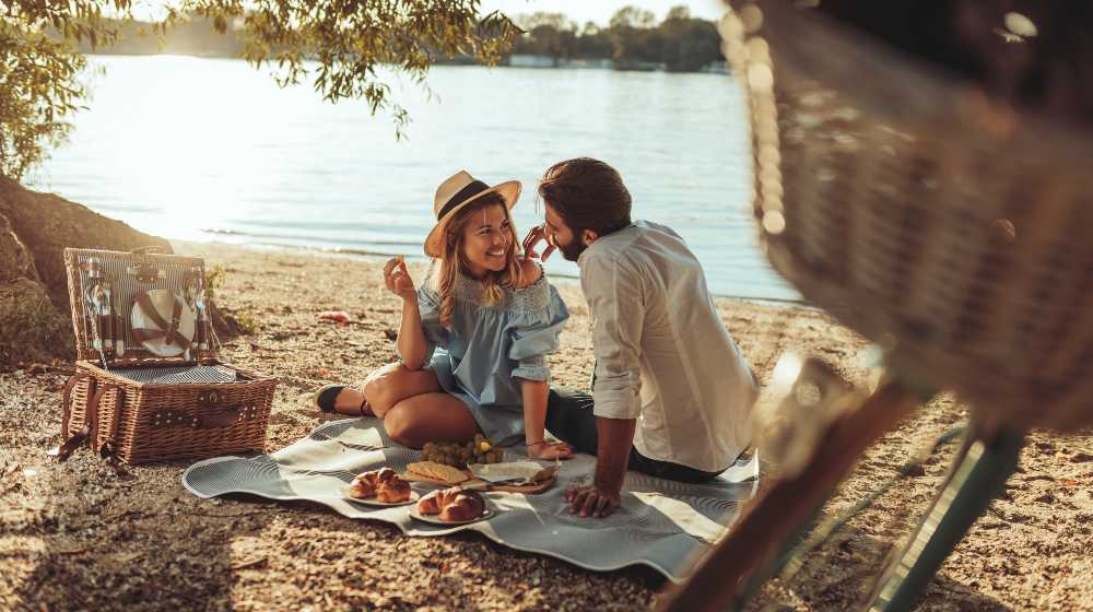 A young couple having a picnic at the beach | What To Bring To A Picnic | featured